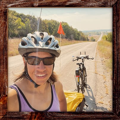 Photo, Day 40 of the TransAmerica Bicycle Trail, Mandy with her bicycle on a hilly road surrounded by farms