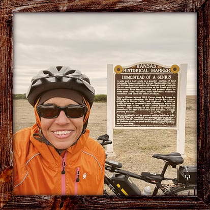 Photo, Day 37 of the TransAmerica Bicycle Trail, Mandy with her bicycle in front of the sign marking the homestead of Gear Washington Carver