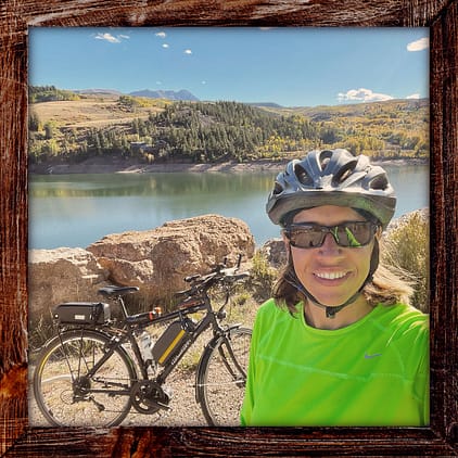 Photo, Day 30 of the TransAmerica Bicycle Trail, Mandy with her bicycle in front of a lake and mountains
