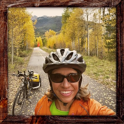 Photo, Day 31 of the TransAmerica Bicycle Trail, Mandy with her bicycle on a bicycle path with golden aspens along the path and mountains in the background