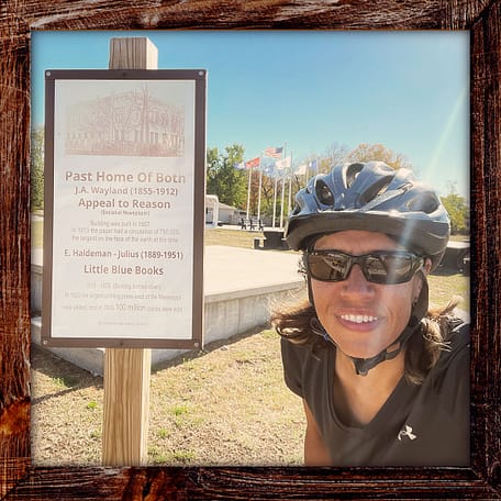 Photo, Day 41 of the TransAmerica Bicycle Trail, Mandy with a sign in Girard Kansas marking the location of the "Appeal to Reason" newspaper and the Little Blue Books printing press