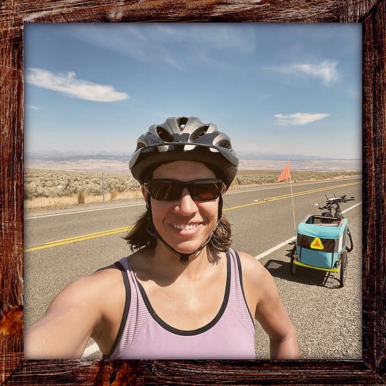 Photo, Day 10 of the TransAmerica Bicycle Trail, Mandy and her bicycle on a vast stretch of open road, dessert, and mountains east of Baker City Oregon